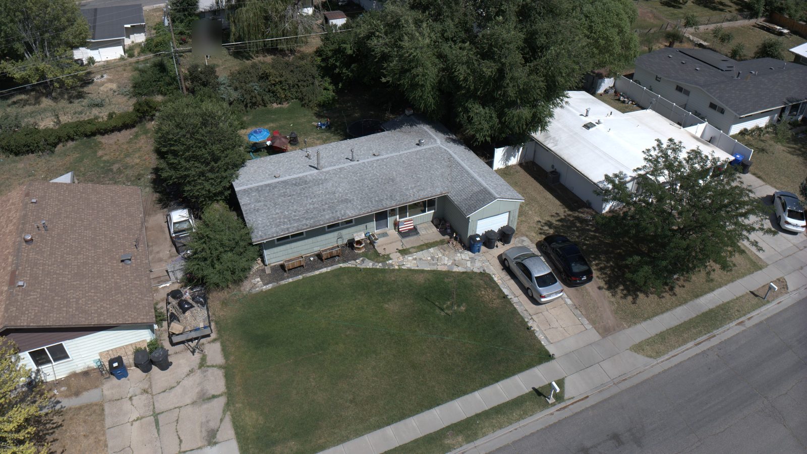 Drone view of a Utah ranch home with a gray shingle roof under mature shade trees
