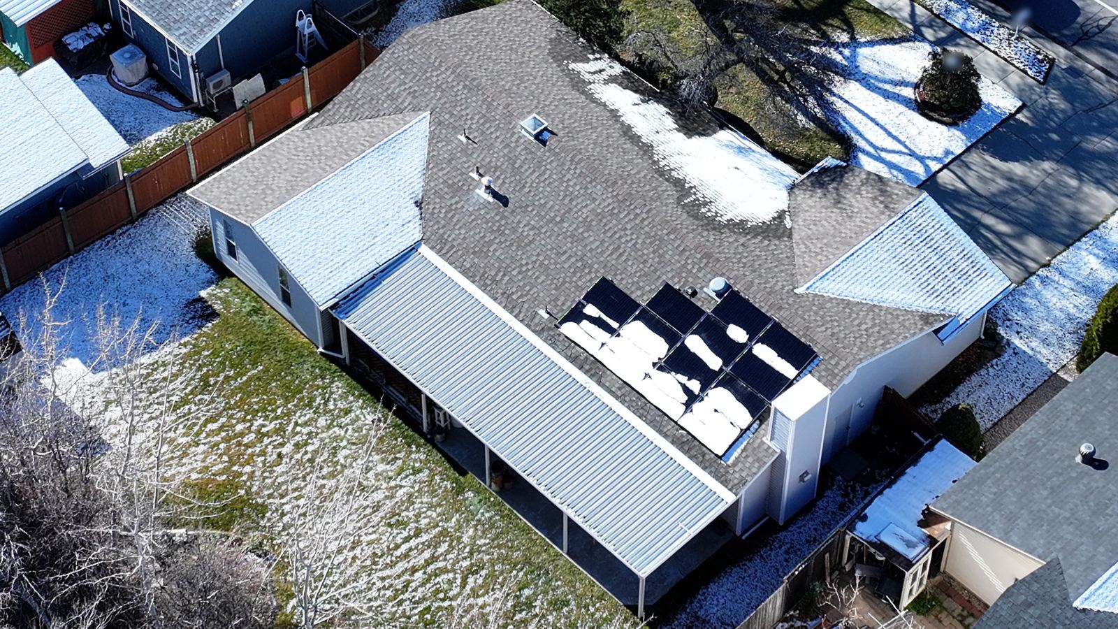 Light snow melting unevenly on a Utah home's asphalt shingle roof in winter