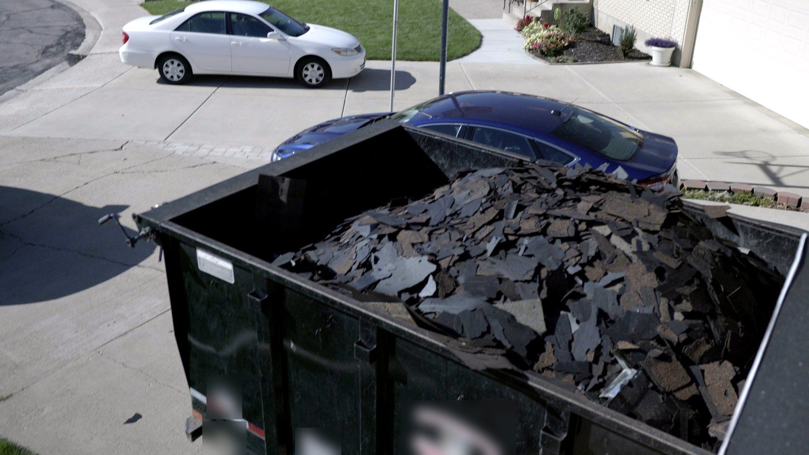 Roll-off dumpster loaded with old asphalt shingles from a roof replacement